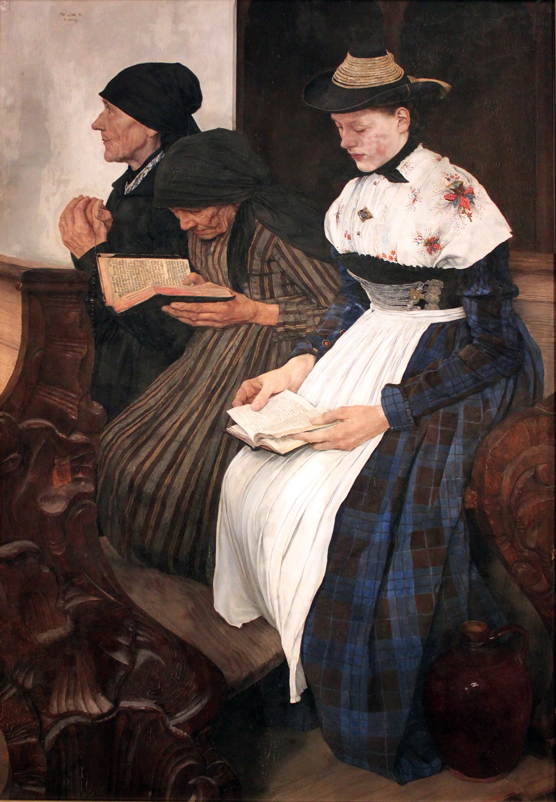 Wilhelm Leibl, 1878–1882, olej - wnętrze wiejskiego kościoła, rzeźbione ciemne drewno ławki i tło niemal bez szczegółów; w jednej ławce siedzą jedna za drugą trzy kobiety w wyraźnie różnym wieku, dwie starsze w czarnych chustkach na głowach i ciemnych strojach, najmłodsza w czarnym kapeluszu ze złotą taśmą, w białej chuście w kwiaty i białym fartuchu na kraciastej sukni; najstarsza z tyłu ma tylko splecione dłonie, środkowa pochyla się nad zniszczonym modlitewnikiem, najmłodsza trzyma otwartą książkę na kolanach, a przy jej spódnicy stoi na podłodze gliniany dzban