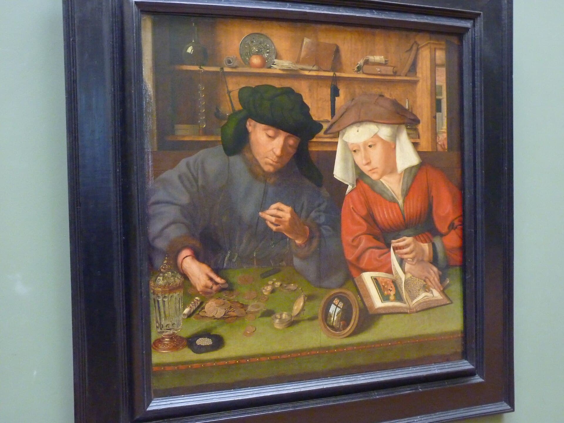 Job Adriaensz. Berckheyde, Dziedziniec starej giełdy w Amsterdamie, ok. 1670 - widok spod ciemnego sklepienia krużganka na kwadratowy dziedziniec wyłożony szachownicą jasnych i ciemnych płyt; po prawej, w ostrym słońcu pod arkadami, stoi gęsty tłum mężczyzn w czarnych płaszczach i szerokich kapeluszach, a pośród nich mężczyzna w białym turbanie i błękitnym kaftanie oraz mężczyzna w długiej żółtej szacie; środkiem pustego bruku idzie dwóch mężczyzn w długich czarnych płaszczach, po lewej dwaj starsi mężczyźni w białych kołnierzach siedzą na kamiennej ławie przy żelaznej barierce, w tle dwukondygnacyjna arkadowa fasada z mansardowymi oknami i skrawkiem nieba