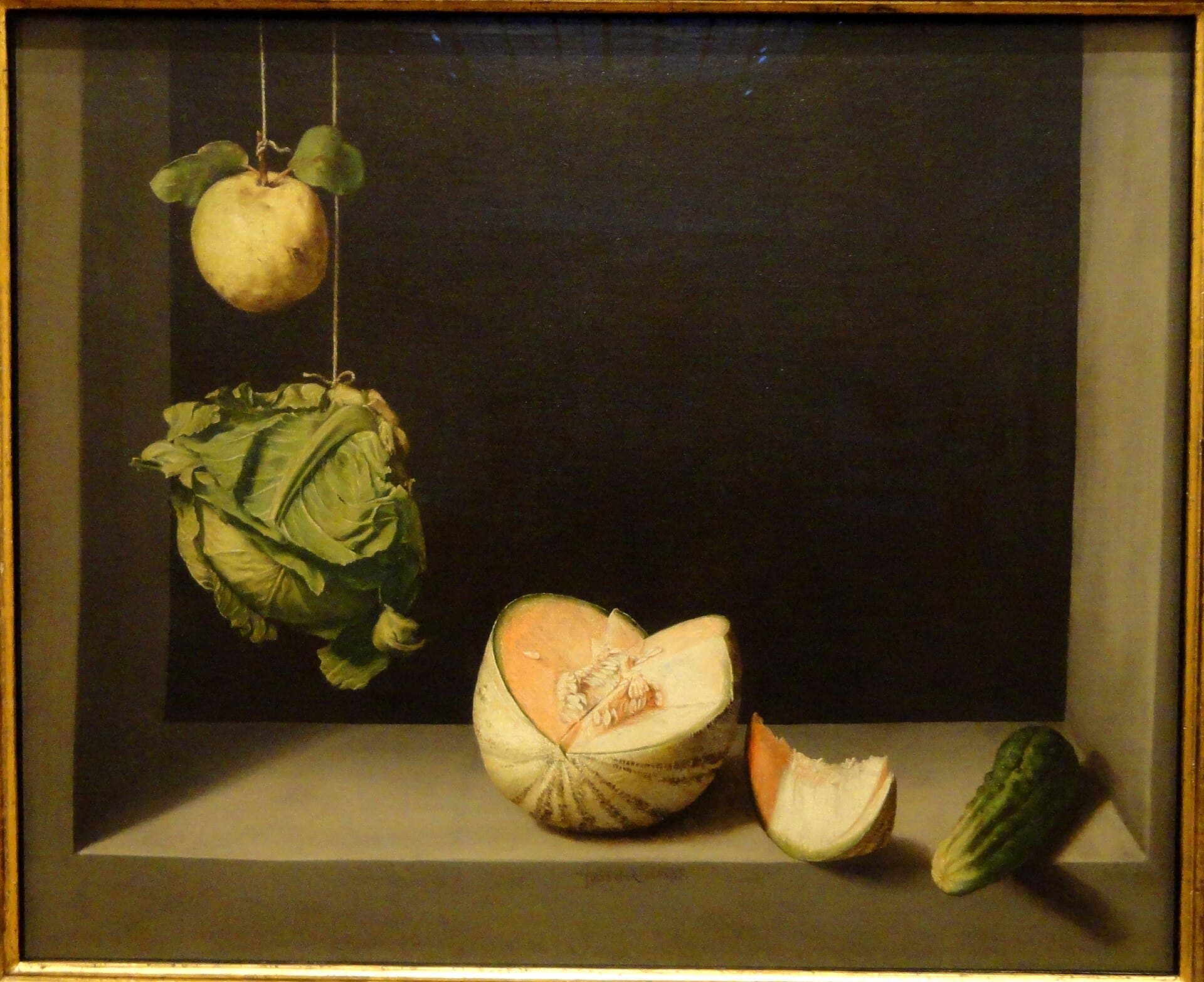 Juan Sánchez Cotán, Pigwa, kapusta, melon i ogórek (ok. 1602, San Diego Museum of Art) — kamienna wnęka o czarnym wnętrzu i jasnym parapecie, oświetlona ostrym światłem z lewej strony. U góry wiszą na dwóch sznurkach żółta pigwa z parą listków i zielona główka kapusty, a na parapecie leżą melon z wyciętym klinem, odkrojona skiba melona i ogórek wysunięty poza krawędź.