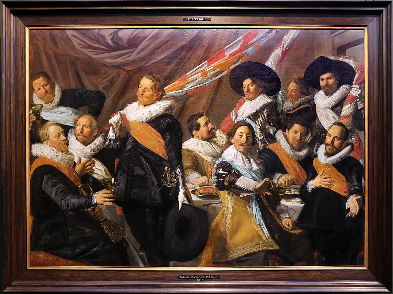 Frans Hals, 1627, olej, Frans Hals Museum w Haarlemie - szeroki portret grupowy kilkunastu mężczyzn stłoczonych wokół długiego stołu nakrytego białym obrusem, na którym stoją talerze i kielichy; wszyscy mają czarne stroje, szerokie białe kryzy pod brodą i barwne szarfy przewieszone przez pierś, jeden unosi kielich, drugi ściska drzewce chorągwi, kilku odwraca się ku sobie w rozmowie, a jeden patrzy poza krawędź obrazu